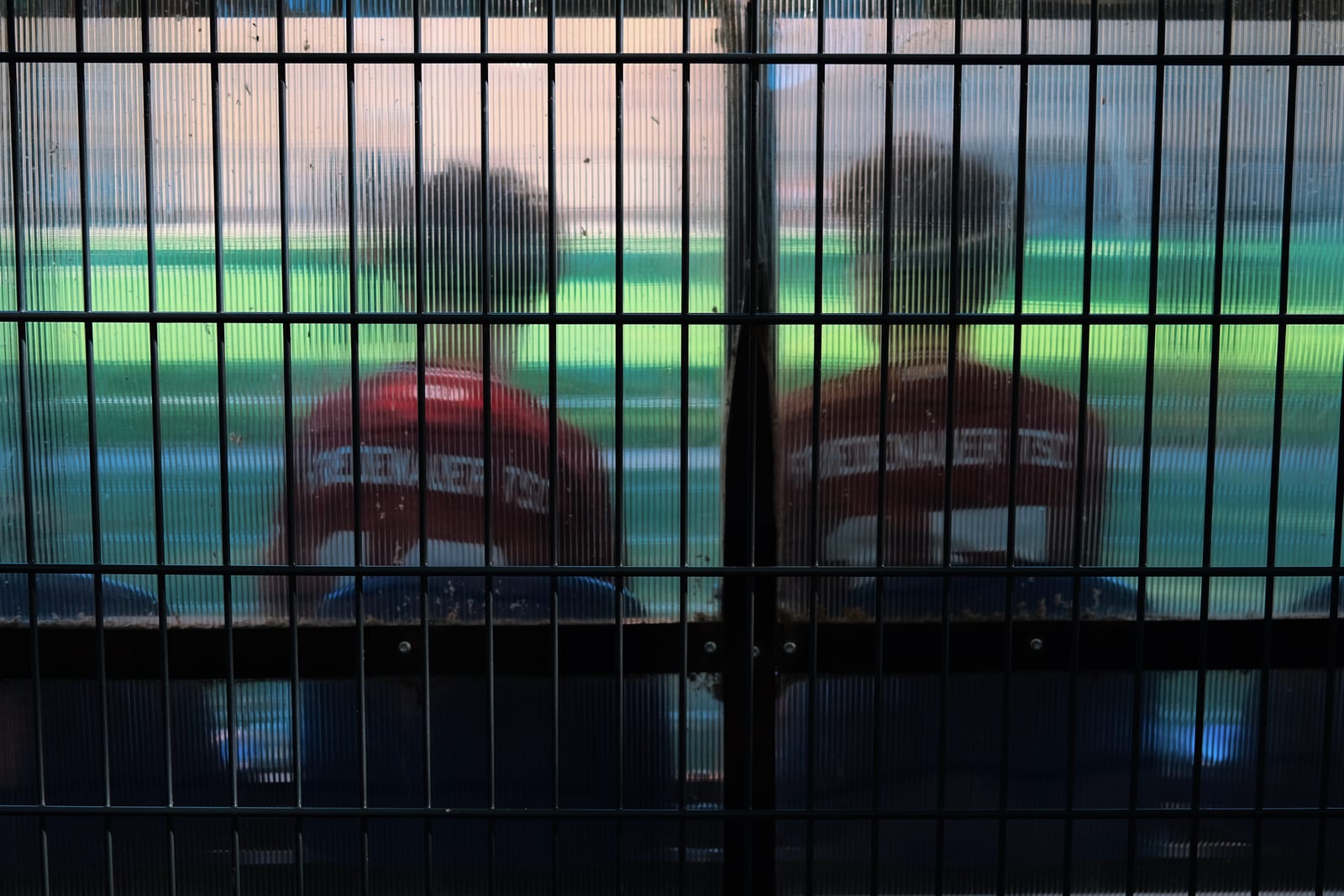 Two figures seen through a mesh fence and a ribbed translucent wall